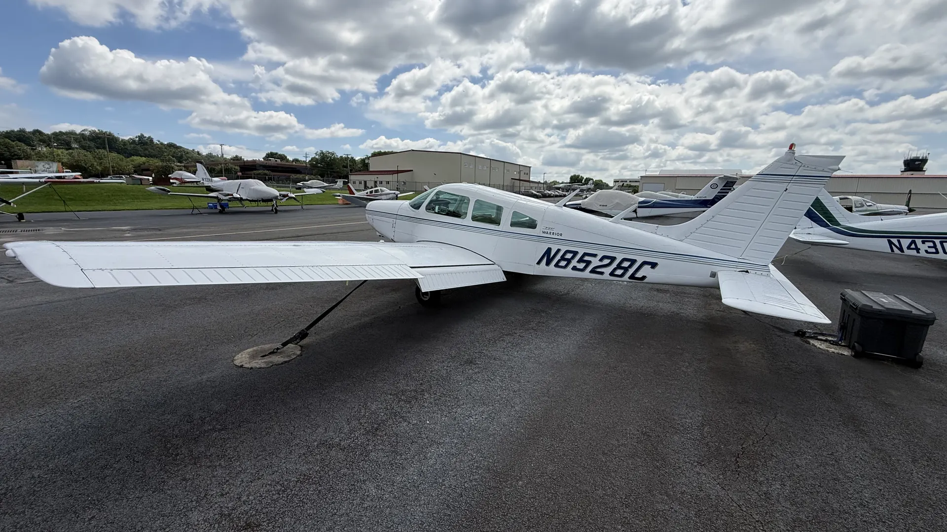 N8528C, a white Piper Warrior, tied down on the ramp at Essex County Airport, seen from above and behind the left wing.