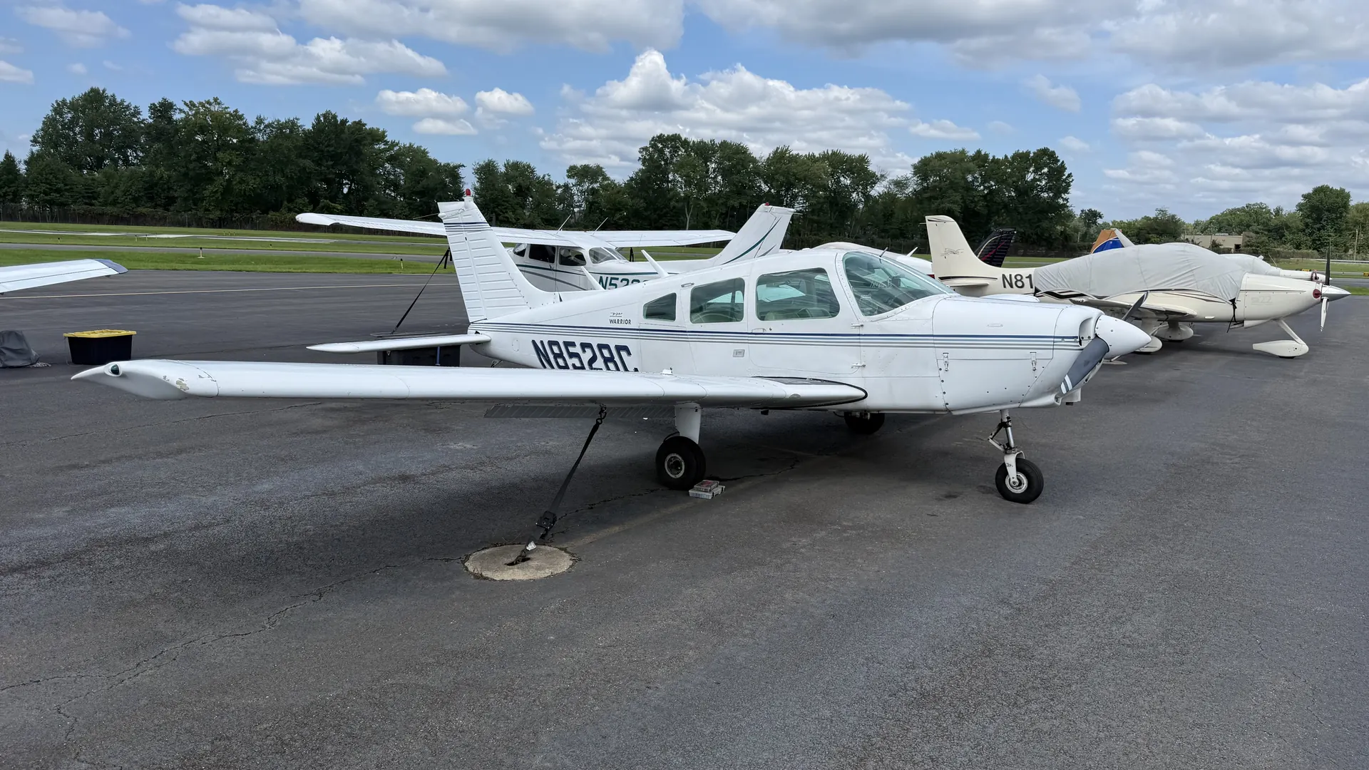 The Warrior from the right side, parked among other light aircraft under a partly cloudy sky.