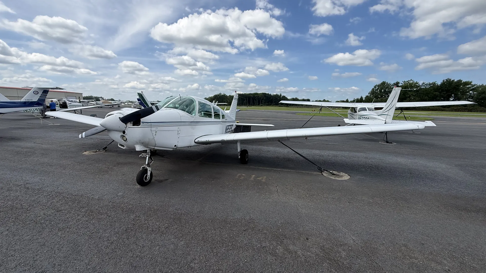 The nose and propeller of the Warrior from the front left, hangars in the background.